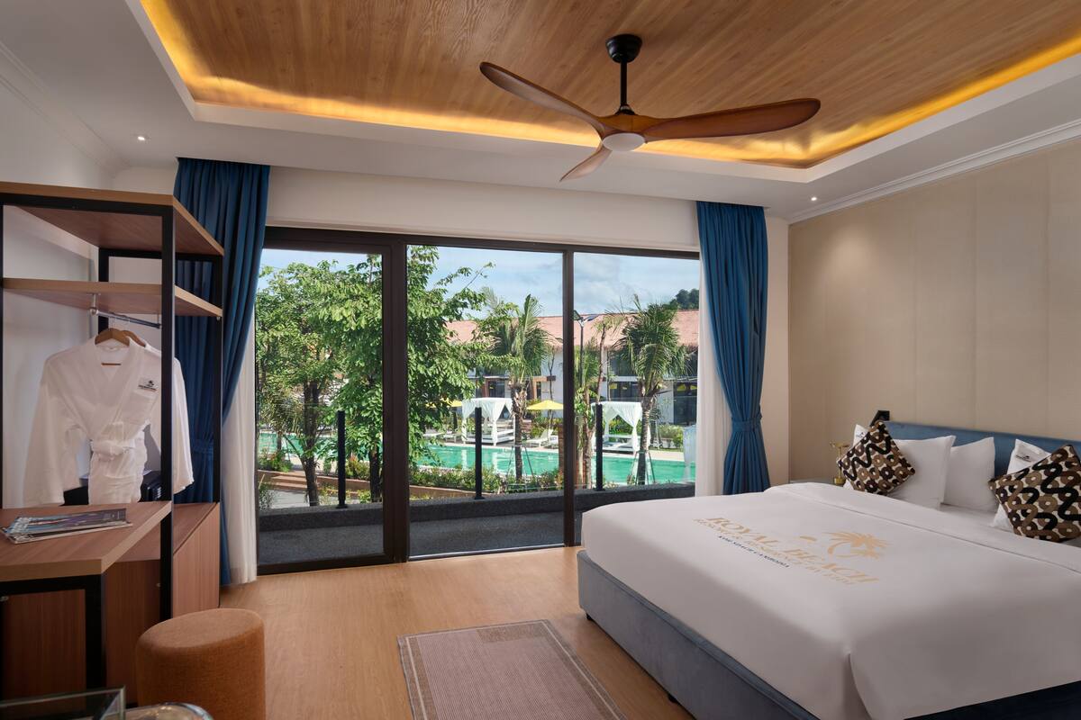 Habitación de hotel con cama, escritorio, armario y vistas a una piscina y follaje.