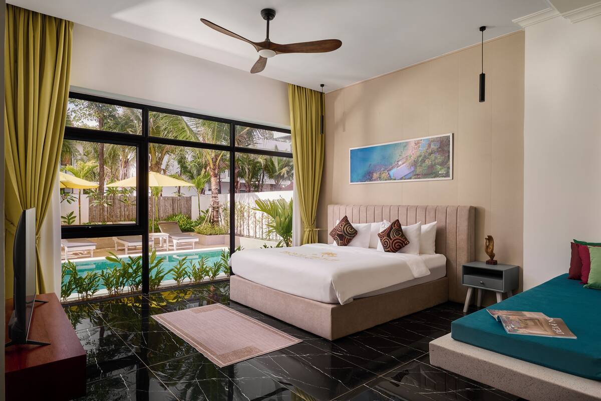 Habitación de hotel con un ventanal grande, una cama, un escritorio y un pequeño balcón con piscina.