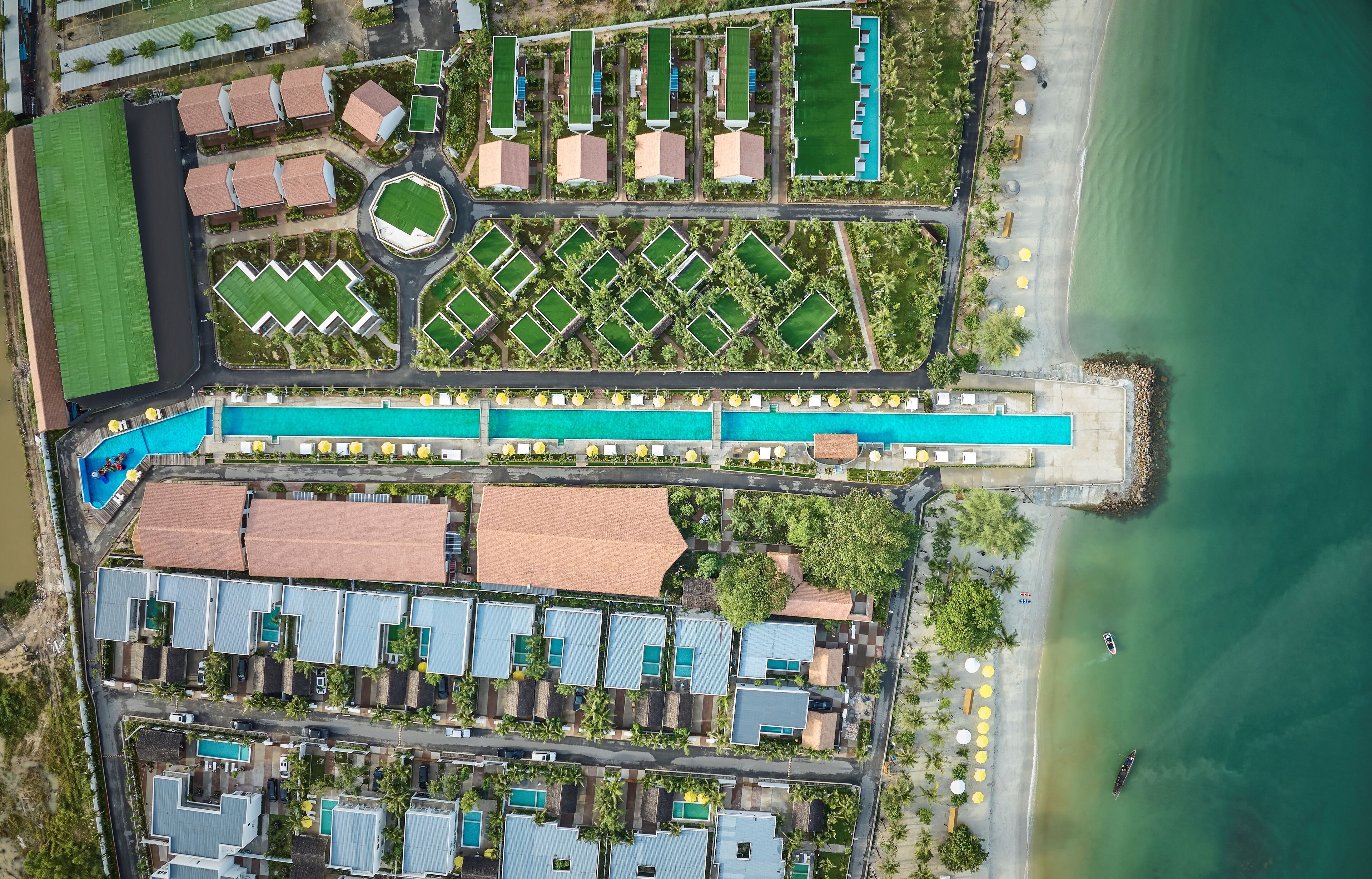 An aerial view of a coastal hotel with multiple swimming pools, a beach, and a marina.