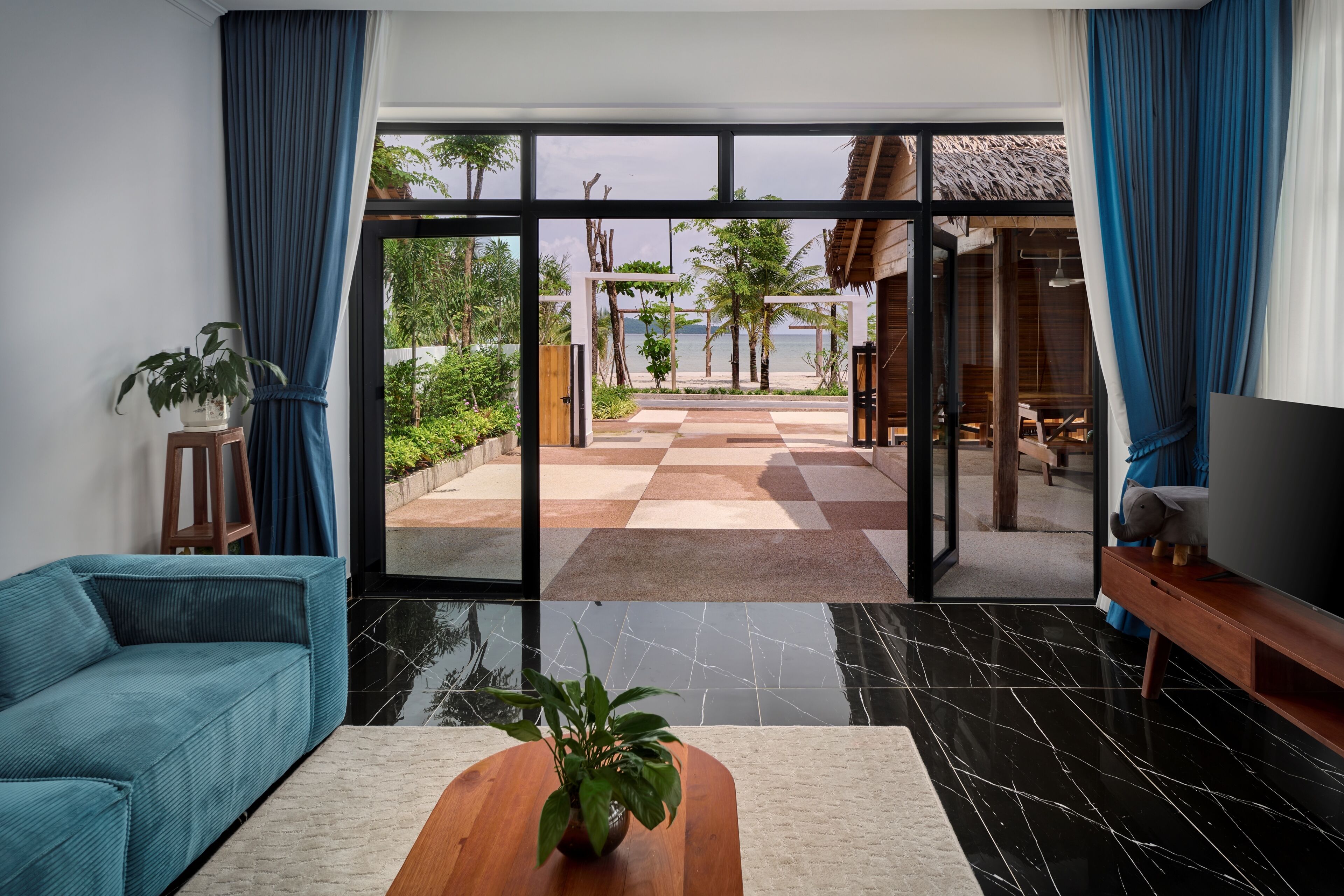 A modern living room with a large glass door leading to a checkered outdoor area with a view of the sea.