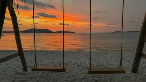 Un columpio de madera en una playa arenosa con un atardecer de fondo.