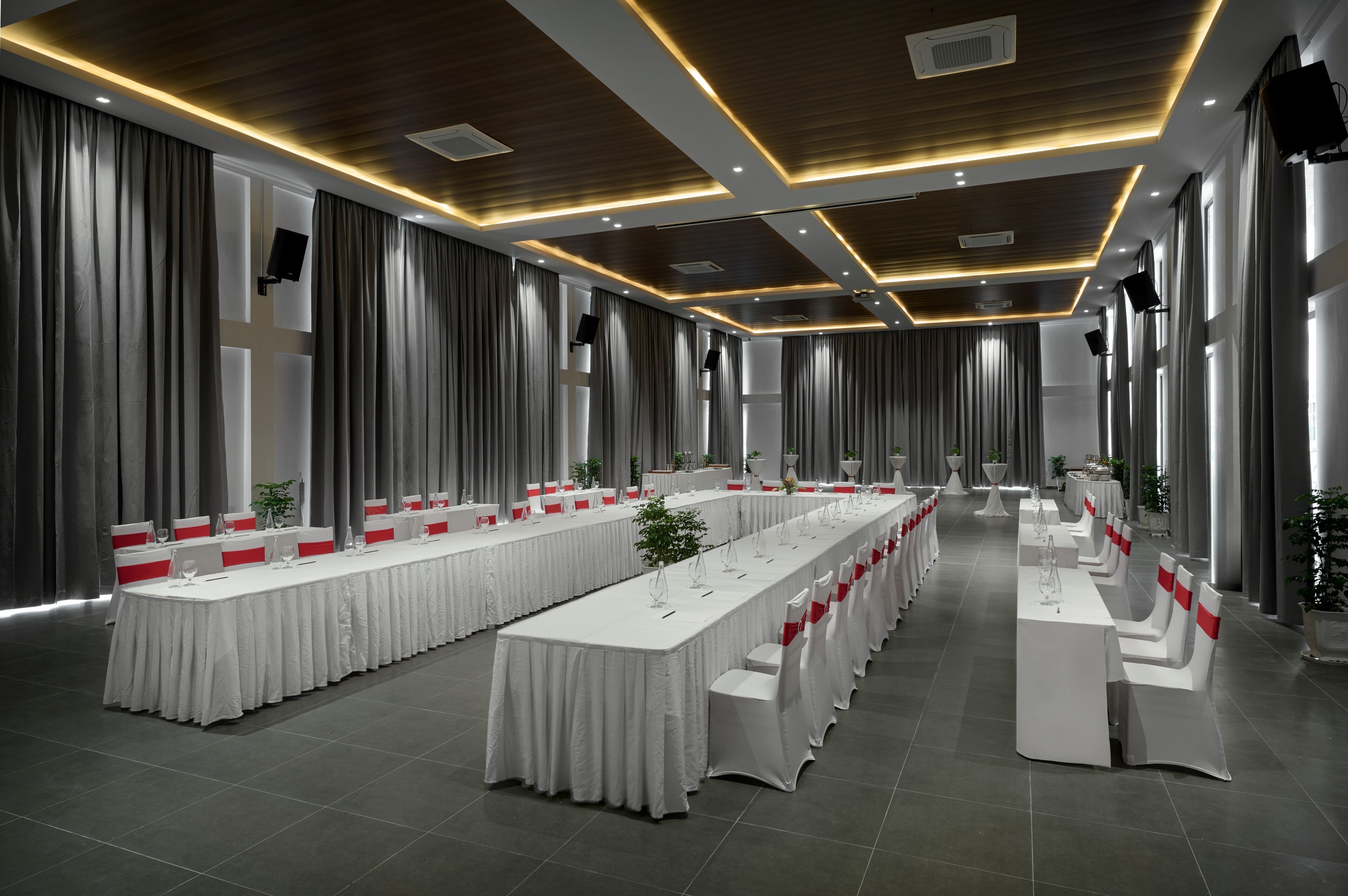 A conference room with long tables, white tablecloths, and red sashes.