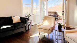 Un salon avec un canapé aux couleurs foncées, un fauteuil aux couleurs claires et une petite table sur laquelle est posée une plante. De grandes fenêtres et une porte-fenêtre coulissante donnent sur un espace patio extérieur.