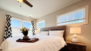 Une chambre avec un grand lit, une table de chevet avec une lampe et une fenêtre avec des stores.