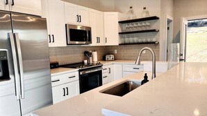 Une cuisine moderne avec des meubles blancs, des appareils en acier inoxydable et un grand îlot central doté d’un évier.