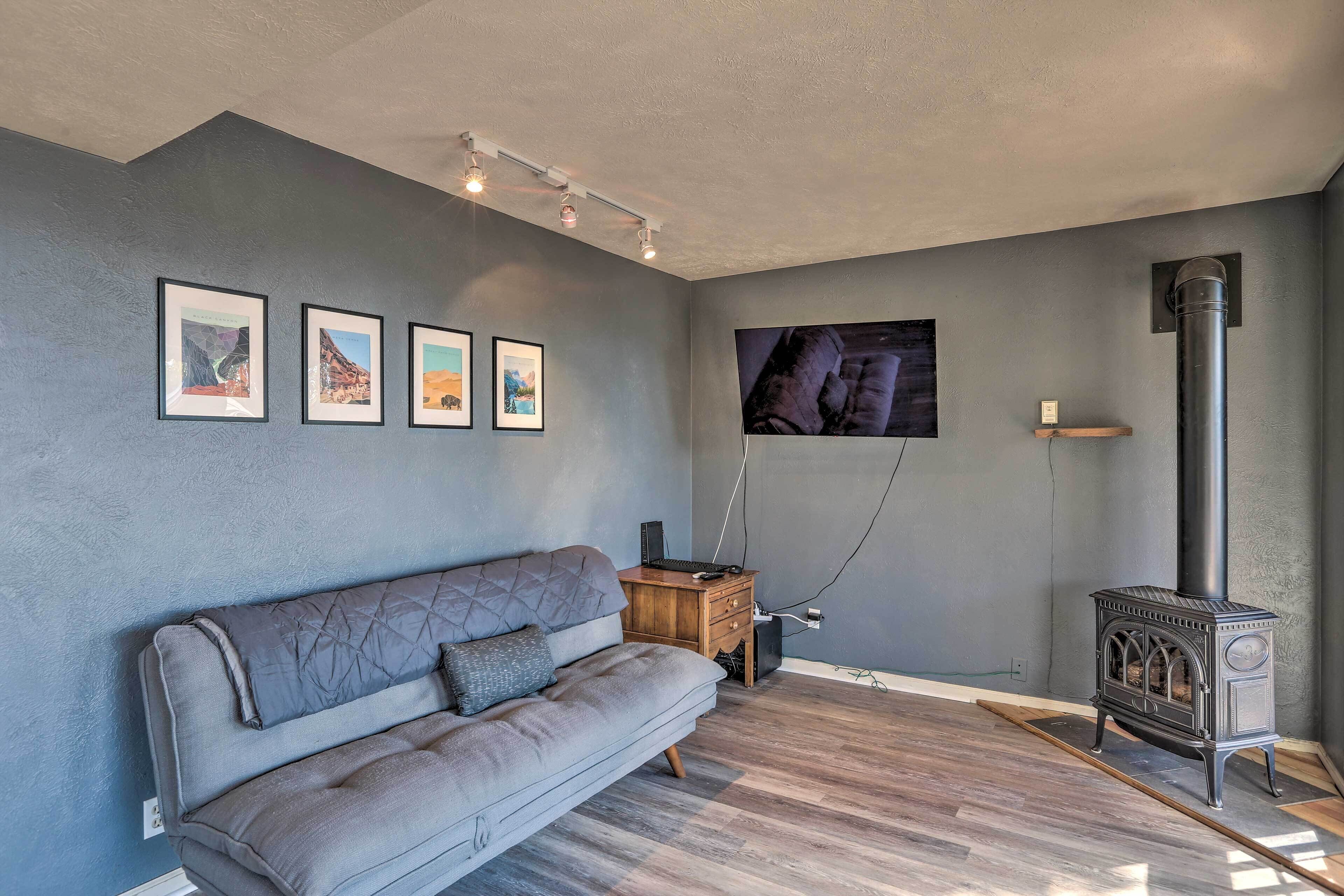 A modern living room with a grey sofa, a wooden side table, a black heater, and framed pictures on the wall.