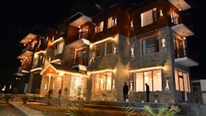 Un hotel de varios pisos con fachada de piedra, múltiples balcones e iluminación exterior cálida.