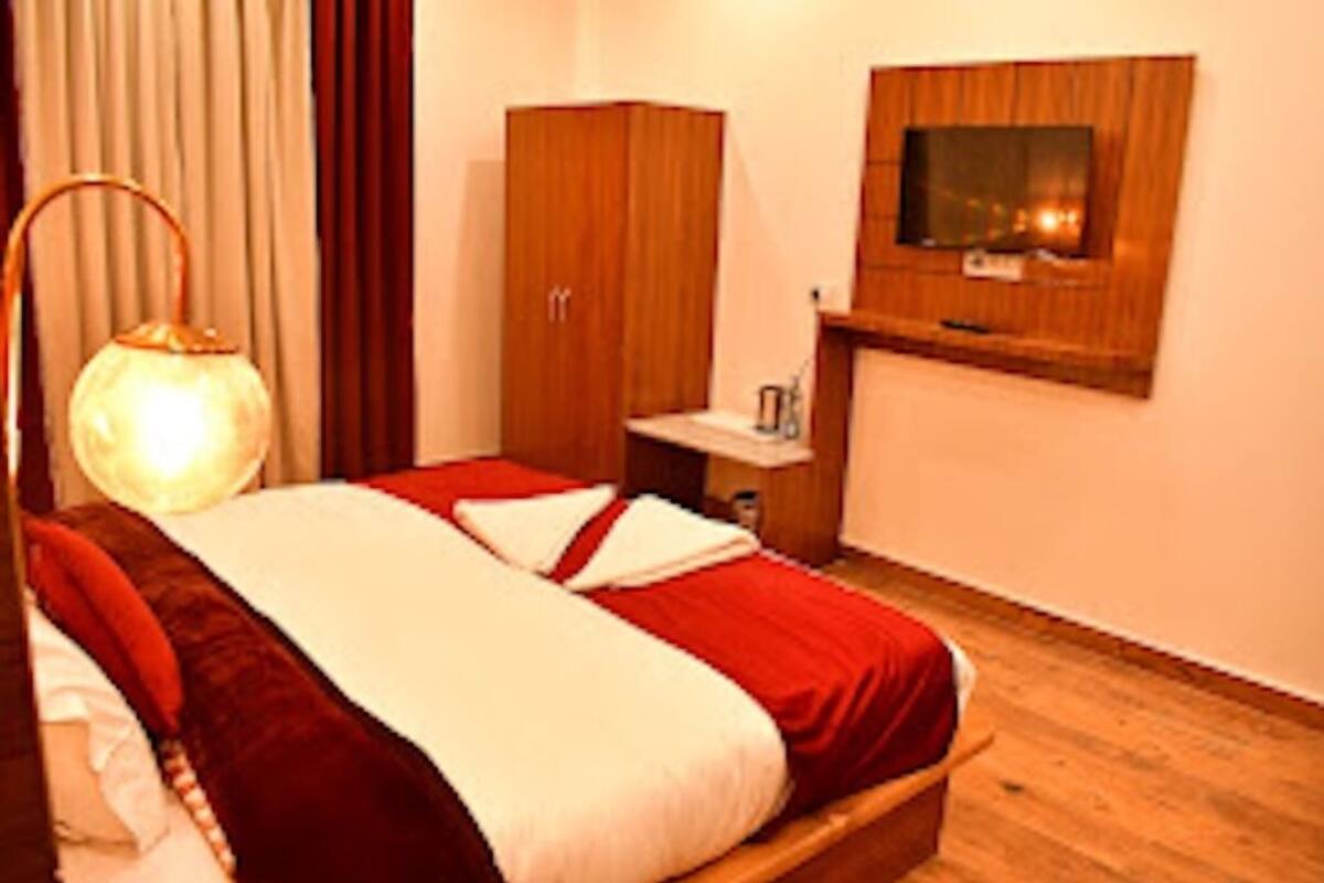 A hotel room with a bed, a wooden wardrobe, a TV mounted on the wall, and a bedside table.