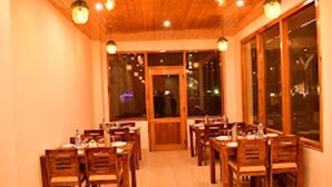 A dining area with wooden tables and chairs, large windows, and a wooden ceiling. - Mountain Majesty Manali (Manali)