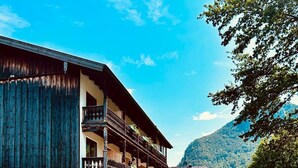 A traditional wooden building with a balcony, a street in front, and a mountain in the background. - Your home in the Bavarian Alps - Spacious vacation on 90 m² with wellness (Flintsbach am Inn)