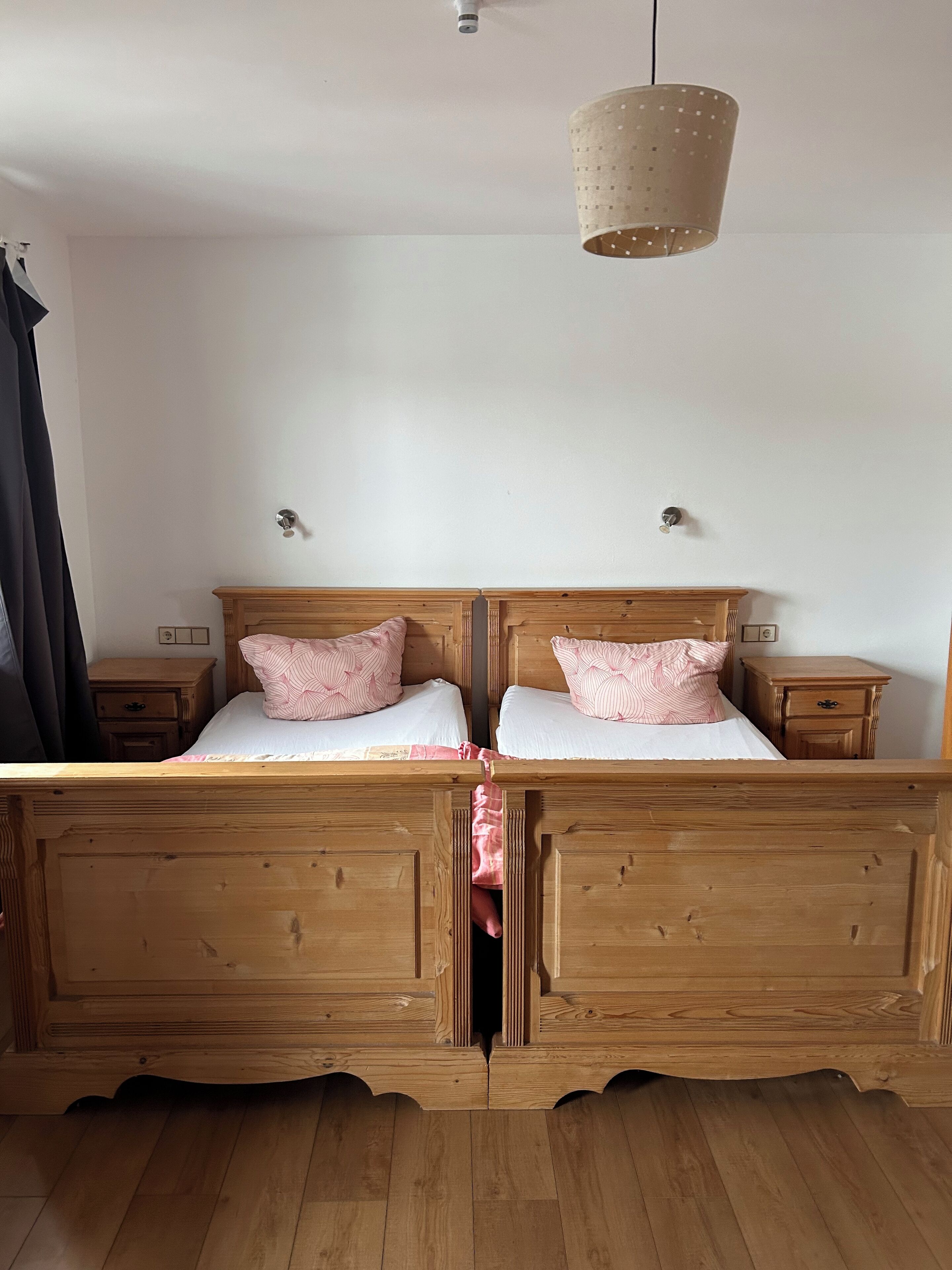 Ein Doppelbett aus Holz mit Kopfteil, zwei Nachttische, eine Pendelleuchte und Holzboden.