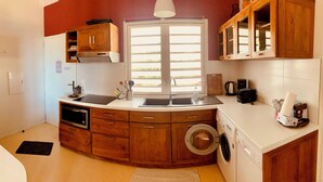 A compact kitchen with a built-in washing machine, wooden cabinets, and a window providing natural light.