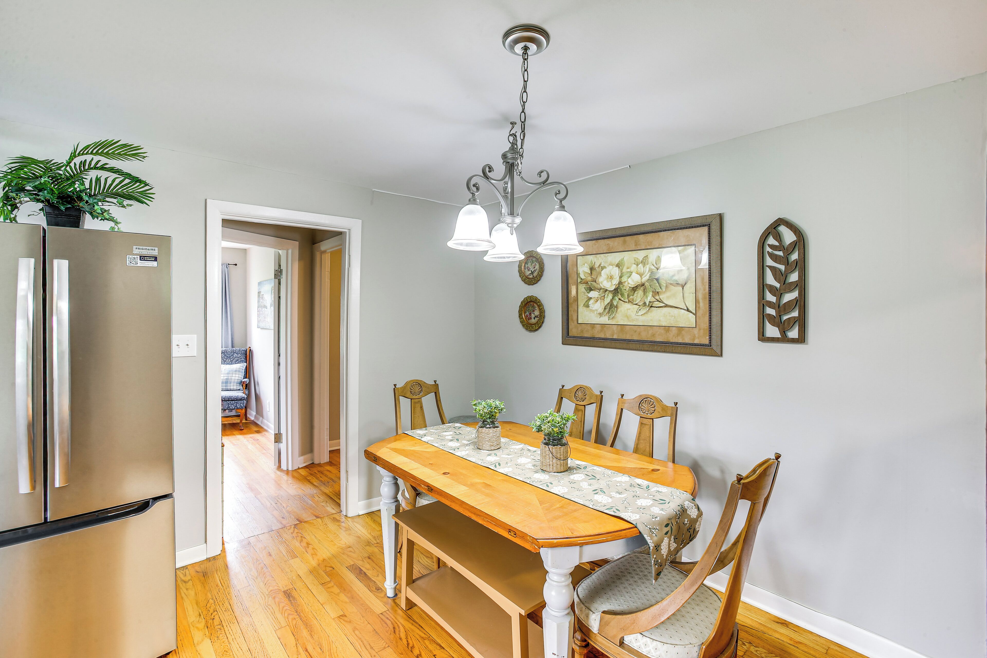A dining area with a wooden table, chairs, a chandelier, and a refrigerator.