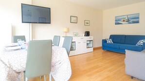 A living room with a TV, a sofa, a dining table with chairs, and a cabinet with a lamp.