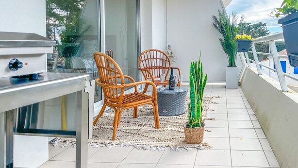 Ein Balkon mit zwei Korbstühlen, einem kleinen Tisch, einem Blumentopf und einer Statue.