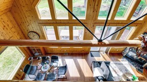 Een houten hut met een eethoek, een woonkamer met een open haard en grote ramen met uitzicht op de omgeving.