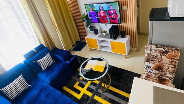 Una sala de estar con un sofá azul, una mesa de centro, un televisor y una cocina al fondo.