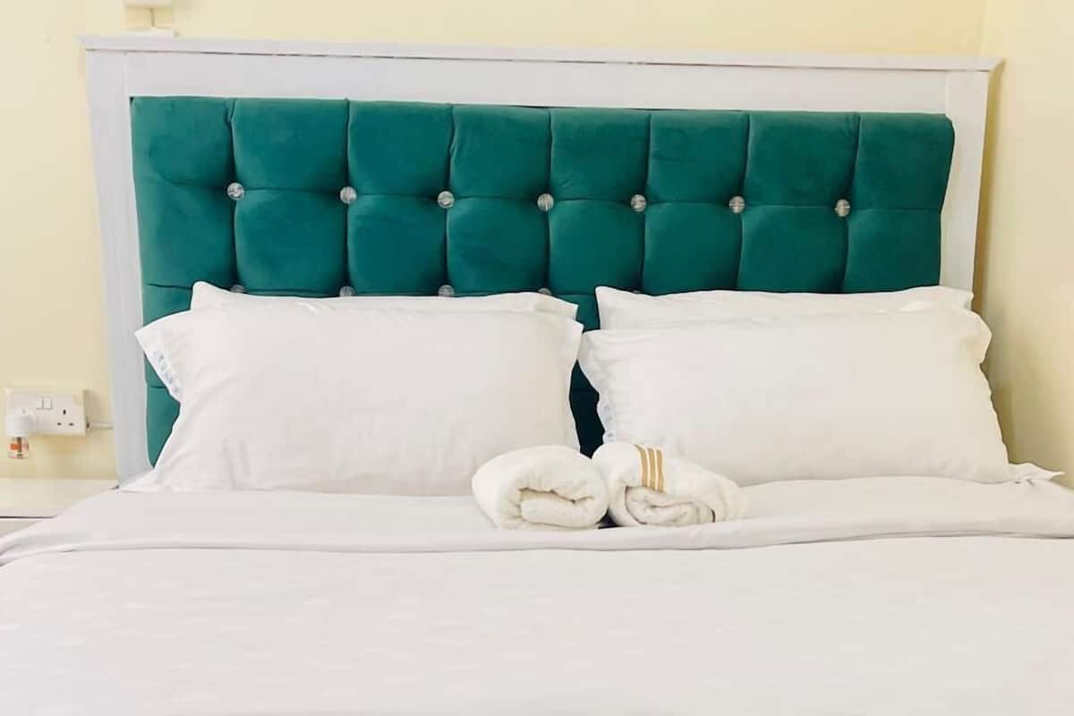 A bed with a teal upholstered headboard and footboard, white bedding, and two rolled towels.