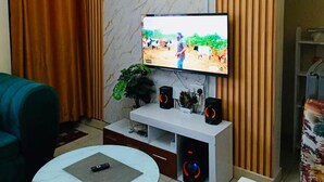 Una sala de estar con un televisor montado en un mueble blanco, un sofá, una mesa de centro y una planta.
