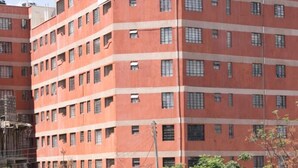 Un edificio de varios pisos con fachada de ladrillo rojo, múltiples ventanas y varios depósitos de agua en el techo.