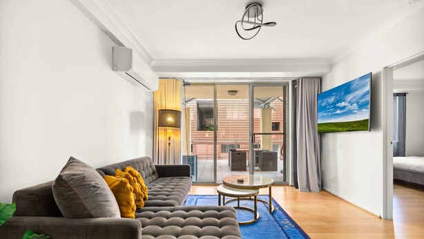 Een moderne woonkamer met een grijze bank, een klein rond tafeltje en een blauw vloerkleed.