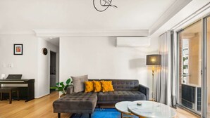 Een moderne woonkamer met een grijze bank, een kleine salontafel en een laptop op een houten vloer.