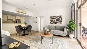 A modern living room with a grey sofa, a coffee table, and a dining area with a black table and chairs.