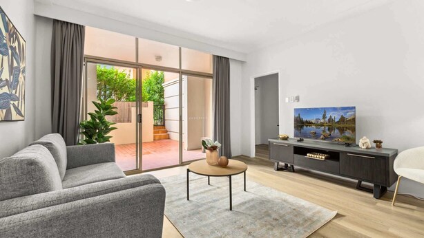 A modern living room with a grey sofa, a coffee table, a flat-screen TV, and a sliding glass door leading to a patio.