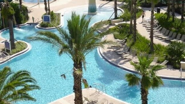 Un área de piscina en un resort, con varias piscinas, palmeras y sillas de descanso.