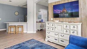 A living room with a TV displaying a castle, a white dresser, two wooden stools, and a blue rug.
