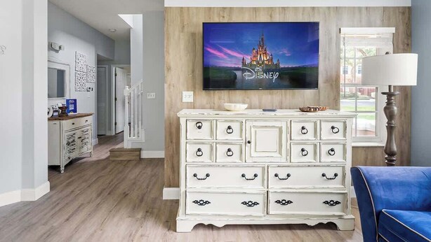 A living room with a white dresser, a flat-screen TV mounted on a wooden wall, and a blue armchair.