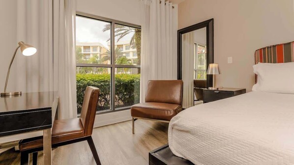 A hotel room with a bed, a desk, a chair, a large window, and a mirror. - Hotel Apt at Celebration 10 min from Disney (Celebration)