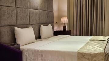 Ett hotellrum med en stor säng, ett vadderat sänggavel, en sänglampa och utsikt över gardinerna.