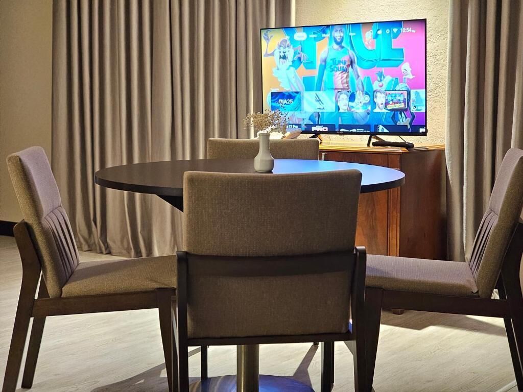 Une salle de conférence équipée d’une table ronde, de quatre chaises, d’un téléviseur à écran plat fixé au mur et d’un meuble en bois.
