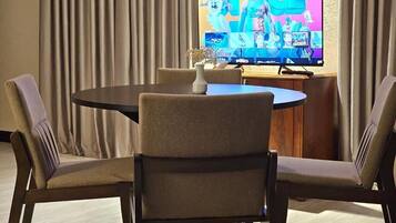 Un salón de conferencias con una mesa redonda, cuatro sillas, un televisor de pantalla plana en la pared y un armario de madera.