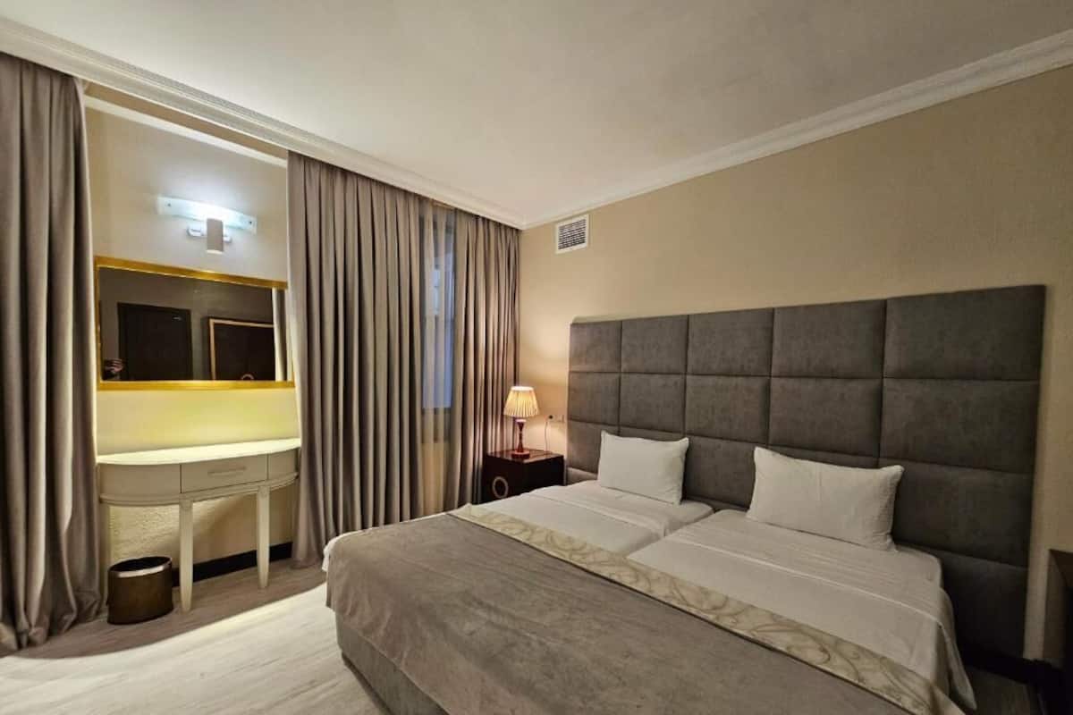 A hotel room with a large bed, a desk with a mirror, and a nightstand with a lamp.