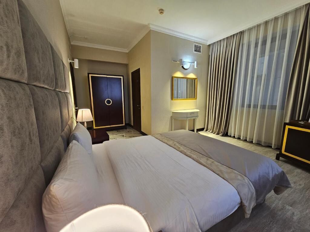 A hotel room with a large bed, a bedside table, a mirror, and a window with curtains.