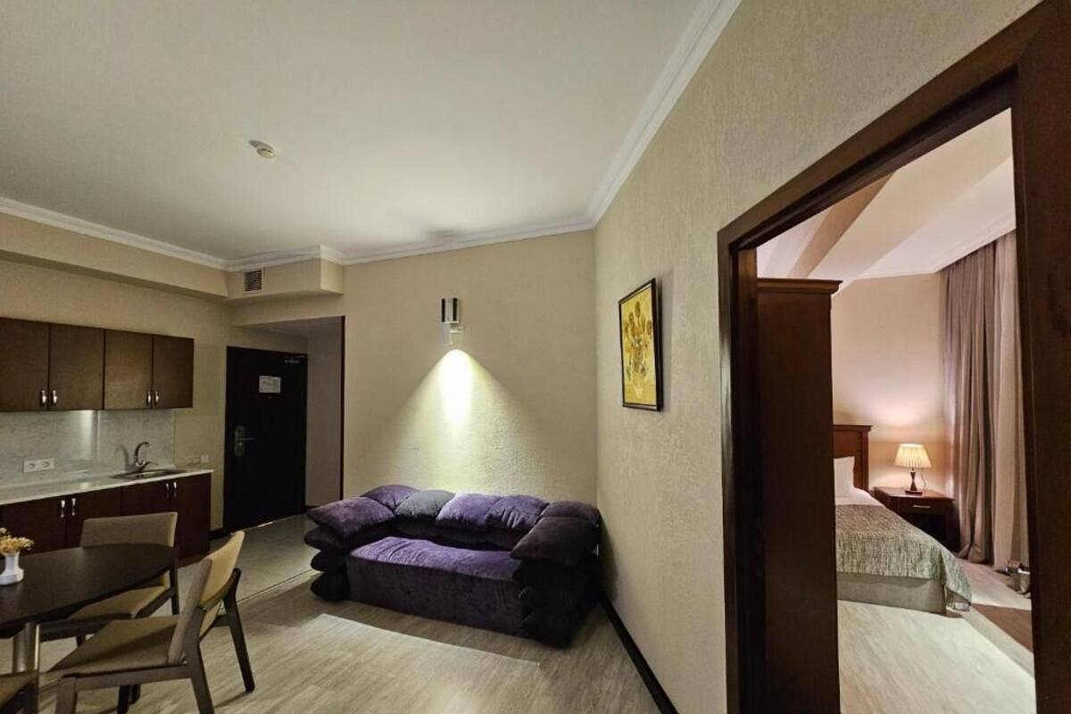 A compact living space with a kitchenette, a sofa, a dining table, and a bedroom with a bed and nightstand.
