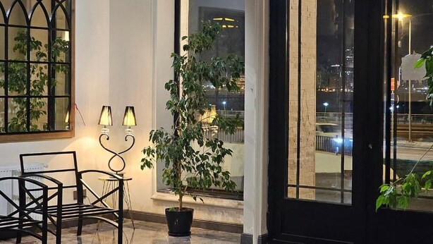 A modern interior with a seating area, a potted plant, and a view of the cityscape through large windows. - Crown Suites Hotel (Baku)