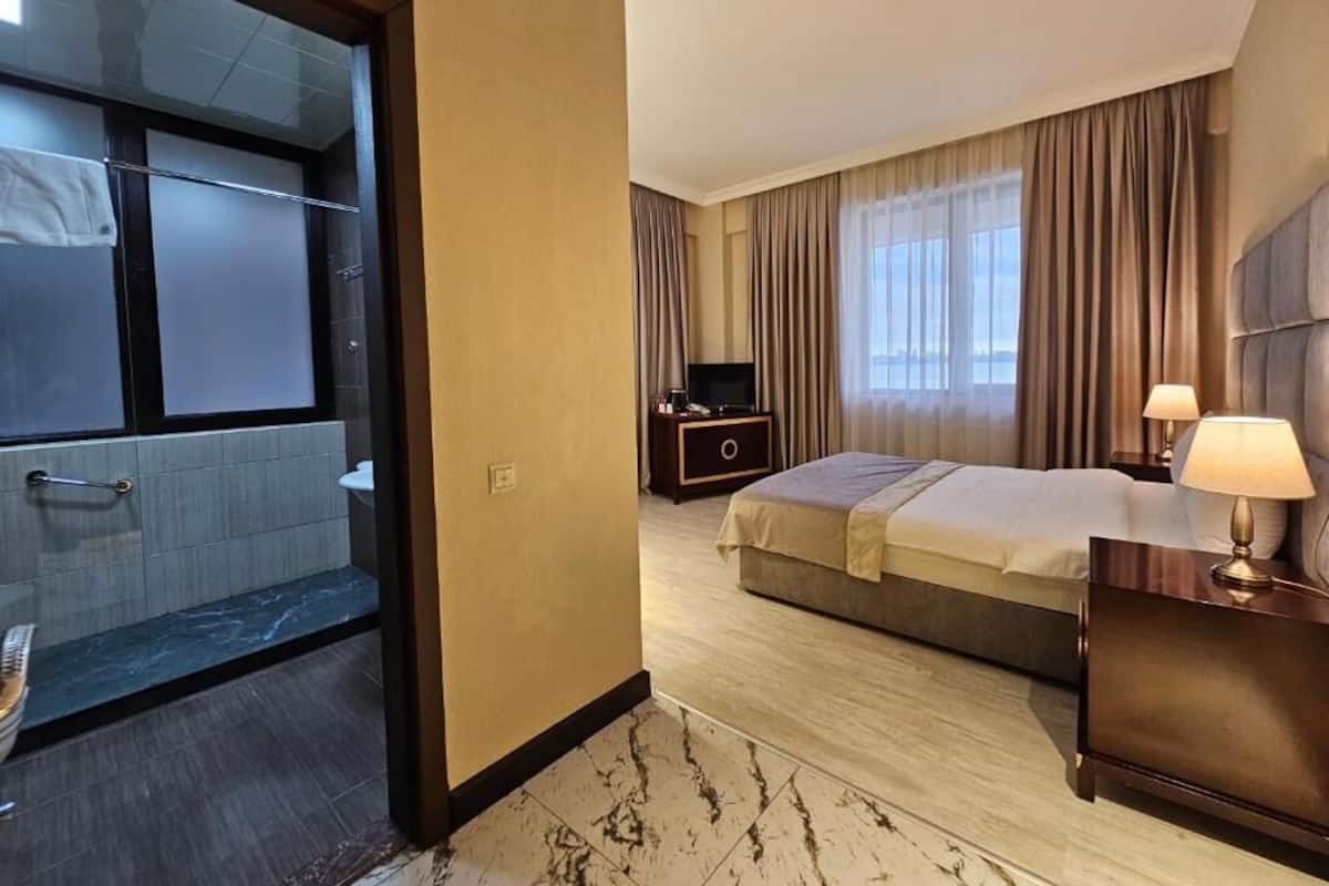 A hotel room with a bed, bedside table, lamp, and a TV.