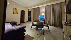 A modern hotel room with a round dining table, two chairs, a sofa, a television, and a large window with curtains. - Crown Suites Hotel (Baku)