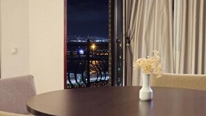 A room with a round table and chairs, a vase with dried flowers, and a view of a cityscape at night. - Crown Suites Hotel (Baku)
