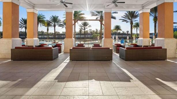 A covered outdoor seating area with multiple sofas and chairs, a pool in the background, and palm trees. - Pet Friendly 4 BR with Hot Tub (Kissimmee)