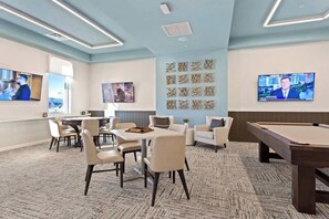 A modern lounge area with a pool table, comfortable seating, and multiple screens displaying news. - Luxury Decor 6BR at Storey Lake sleeps 16 (Kissimmee)