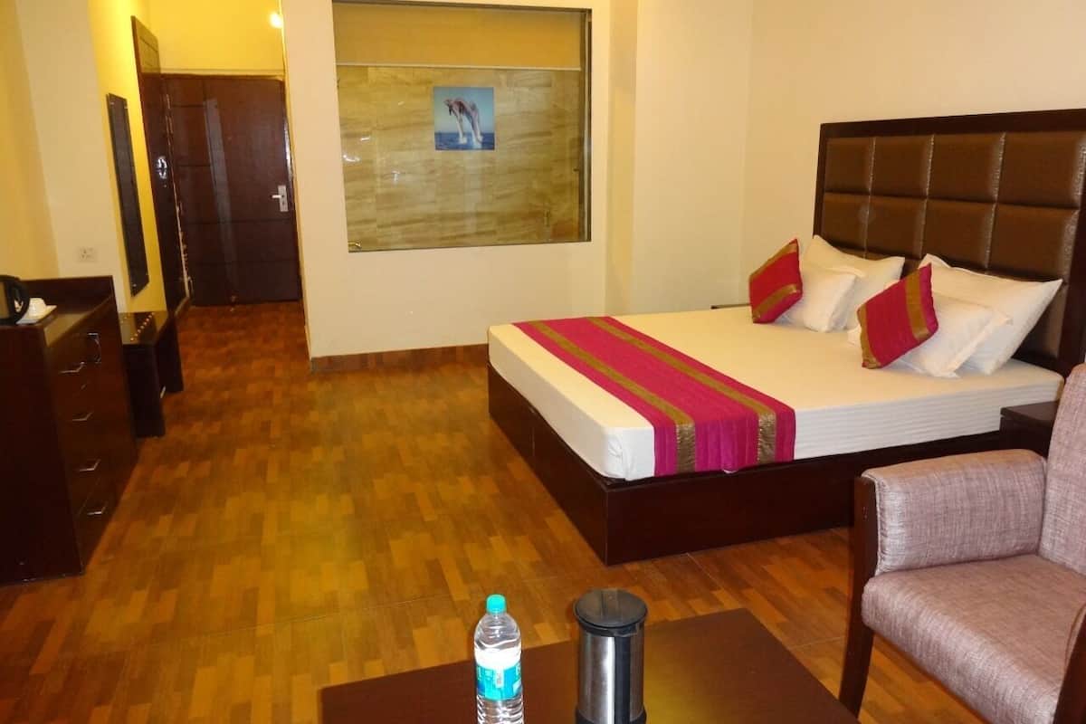 A hotel room with a bed, a chair, a table, a water bottle, and a thermos.