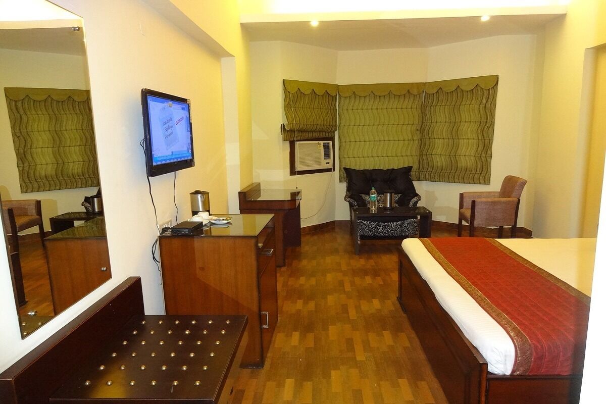 A hotel room with a bed, a desk, a chair, a TV, and a window with curtains.