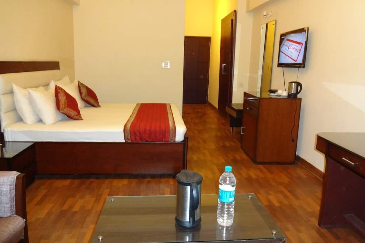 A hotel room with a bed, a coffee maker, a water bottle, and a TV on the wall.