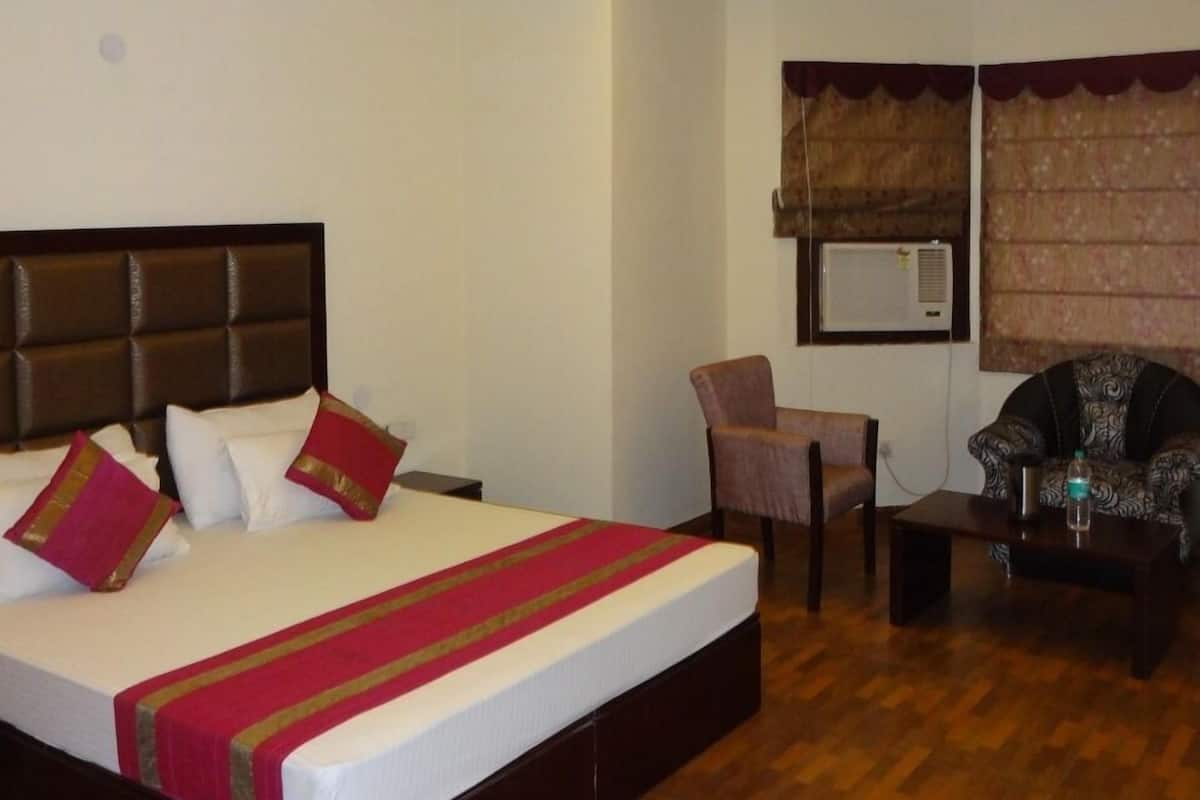 A hotel room with a large bed, a ceiling fan, a chair, a sofa, and a small table.