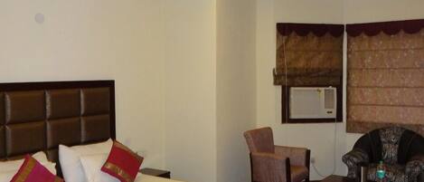 A hotel room with a large bed, a ceiling fan, a chair, a sofa, and a small table.