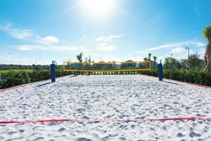 Un terrain de beach-volley sablonneux, avec un filet, entouré de verdure et de palmiers.